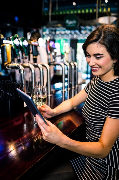 タブレットを使用して、バーでワインのグラスを持つ女性