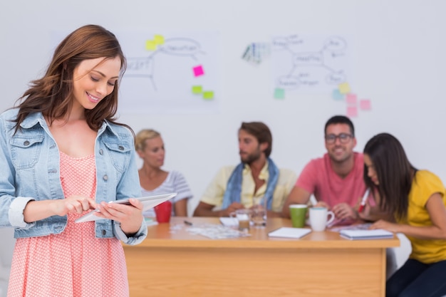 Photo woman using tablet with creative team working behind her