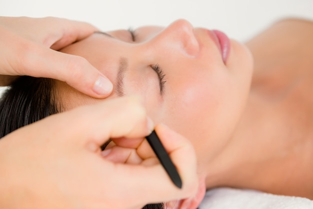 Woman using tweezers on patient eyebrow