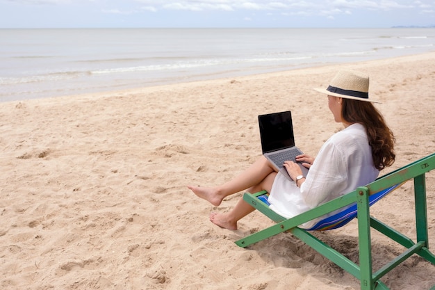 A woman using and typing on laptop computer while lying down on a beach chair