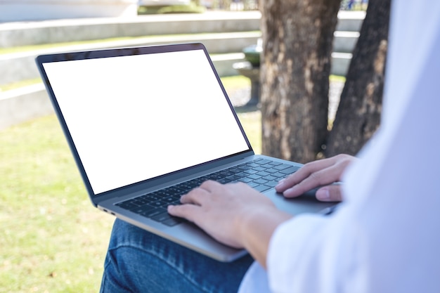 woman using and typing on laptop with blank white screen sitting in the park