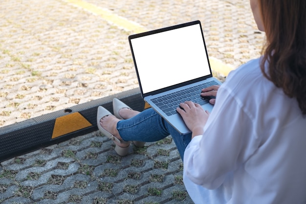 woman using and typing on laptop with blank white screen , sitting in the parking lot outdoors