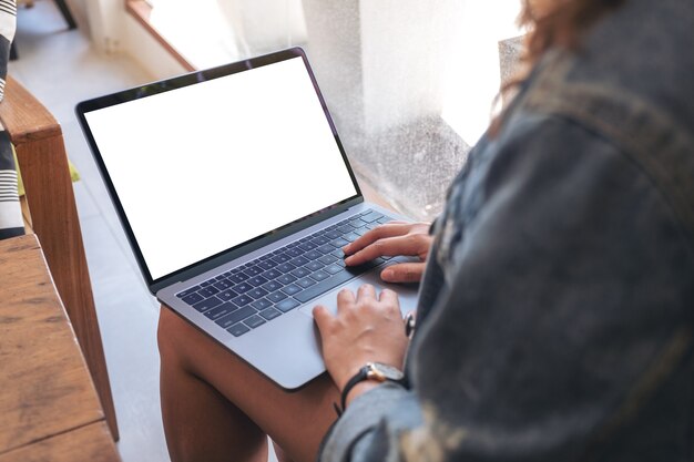 woman using and typing on laptop with blank white screen while sitting in cafe