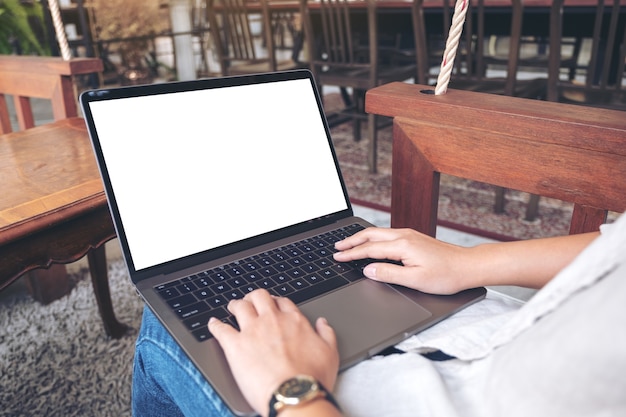 woman using and typing on laptop with blank white screen while sitting in cafe