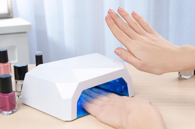 Woman using UV lamp for manicure at table