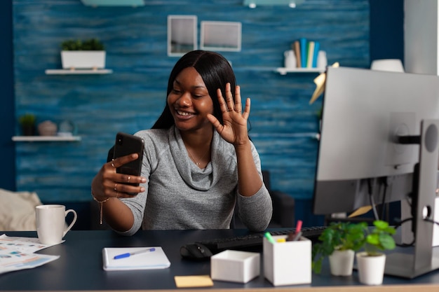 Woman using video call to talk to colleagues from home. Entrepreneur doing business meeting on smartphone with online video conference, waving at mobile phone camera. Remote work