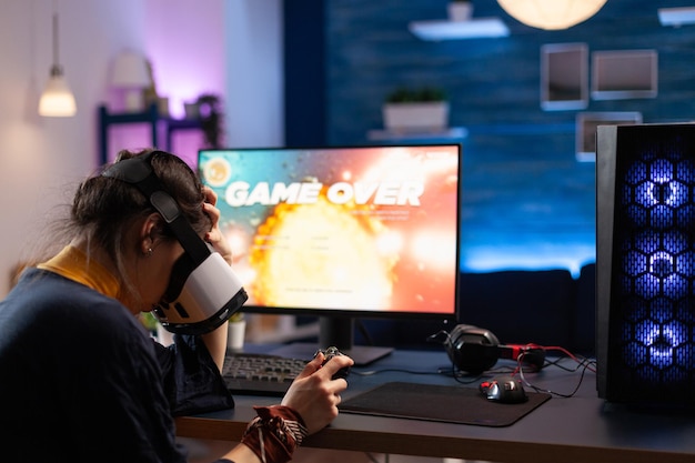 Woman using vr glasses to play online video games and losing on computer. Person playing game with controller on monitor and virtual reality headset. Adult with gaming equipment.