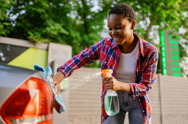 Woman using window cleaner spray, hand car wash station. Car-wash industry or business. Female person cleans her vehicle from dirt outdoors