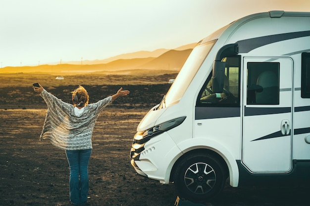 Woman viewed from back enjoy happy her destination in campe van\
life travel back view of female people opening arms and enjoy\
sunset landscape and freedom independence and alternative home\
vehicle