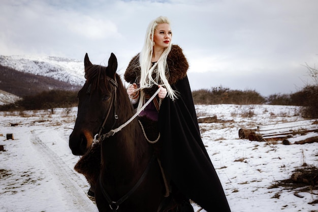 Woman viking with a black horse against the background of mountains