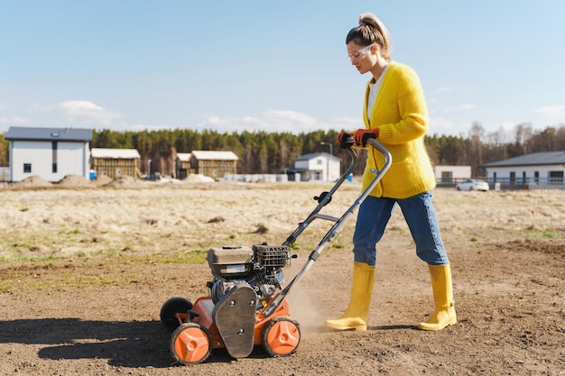 Photo woman villager is using aerator machine to scarification and aeration of lawn or meadow