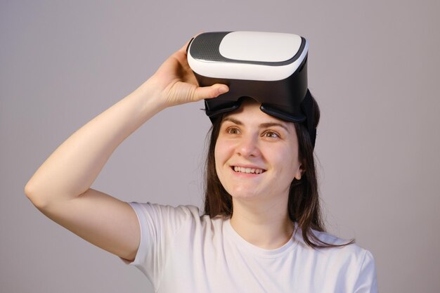 A woman in virtual reality glasses looks up against a gray background