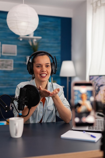 Woman vlogger recording live stream podcast on smartphone.\
influencer talking in front of mobile phone camera and filming\
video for social media channel, using microphone and\
headphones.