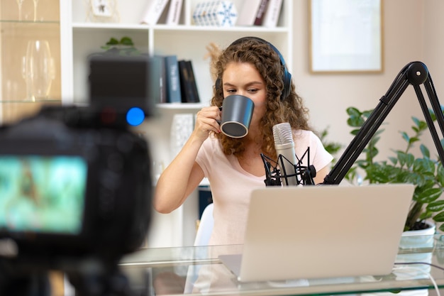 Woman vlogger with headphones looking at laptop and recording video on professional camera