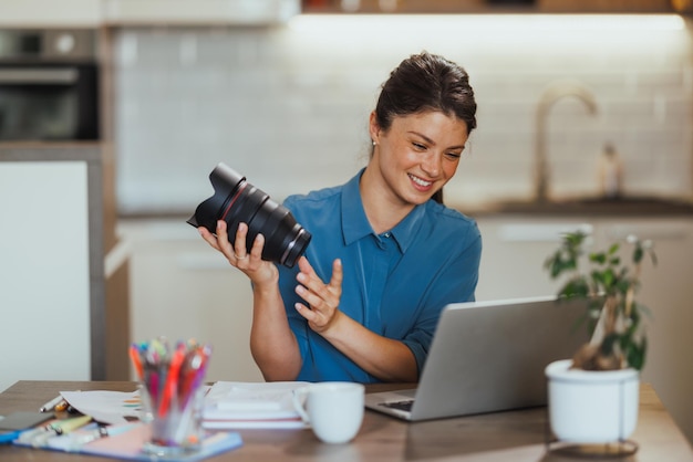 Фото Женщина ведет влог о фотографических продуктах и показывает объектив для камеры во время видеозвонка из своего домашнего офиса