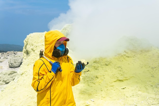 Woman volcanologist on the background of a smoking fumarole examines a sample of a sulfur mineral