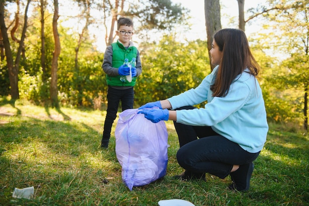 女性ボランティアと男の子がプラスチックごみを拾い、屋外で生分解性のゴミ袋に入れています。生態学、リサイクルおよび自然保護の概念。環境を守ること。