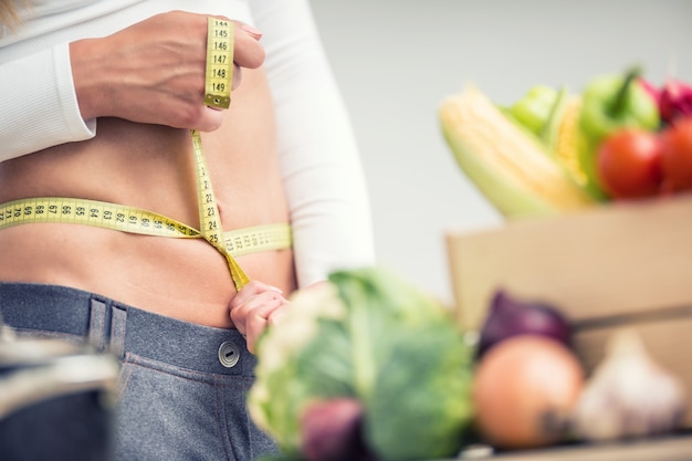 woman waist with measuring tape over wooden box with vegetable.