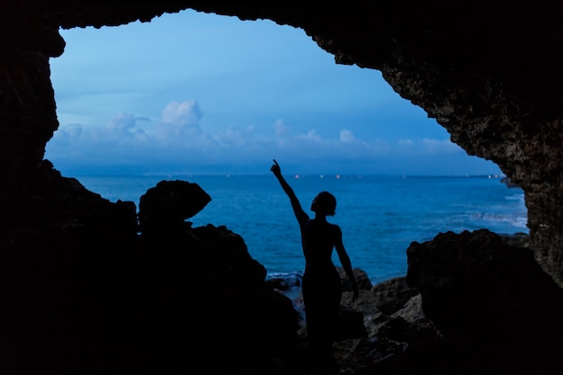 Tramonto di attesa della donna nella caverna di balinesse alla spiaggia dell'oceano.