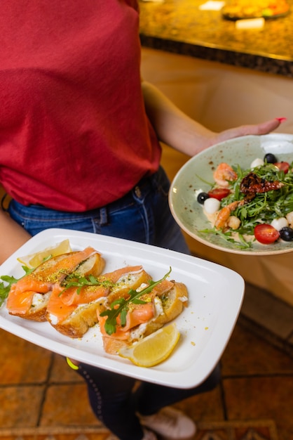 Woman waiter holding a wooden tray with bruschetta in her hand.