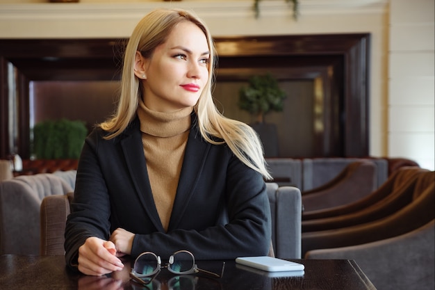 woman waiting for the menu and looking away from the camera. glasses, phone on the table.