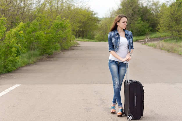 Woman waiting with her suitcase in the road