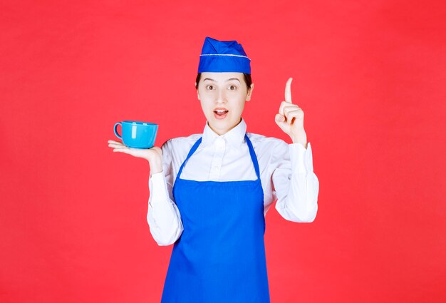 Woman waitress in uniform holding a bowl and pointing up on red wall.