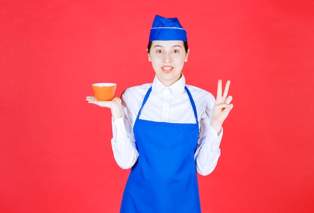 Woman waitress in uniform holding an orange bowl and showing victory sign .