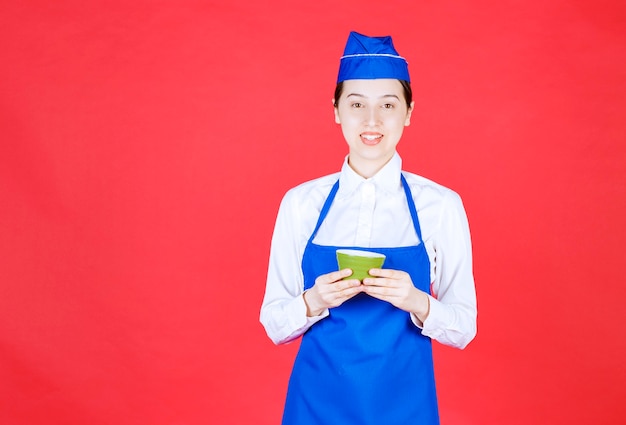 Woman waitress in uniform standing and holding a green bowl .