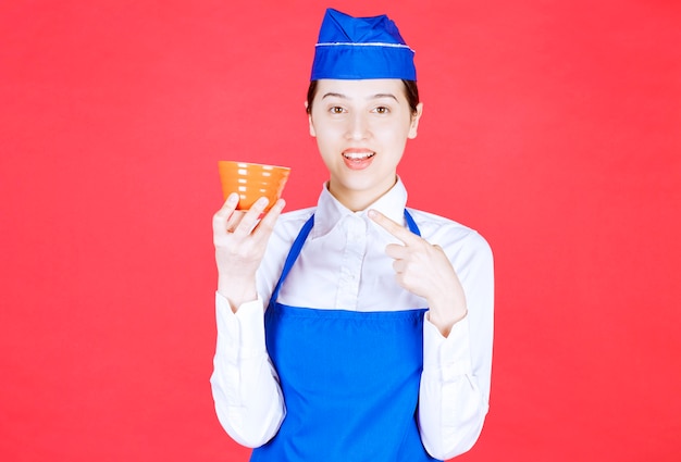 Woman waitress in uniform standing and pointing at an orange bowl .