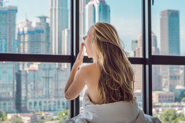 Woman wakes up in the morning in an apartment in the downtown area with a view of the skyscrapers. Life in the noise of the big city concept. Not enough sleep