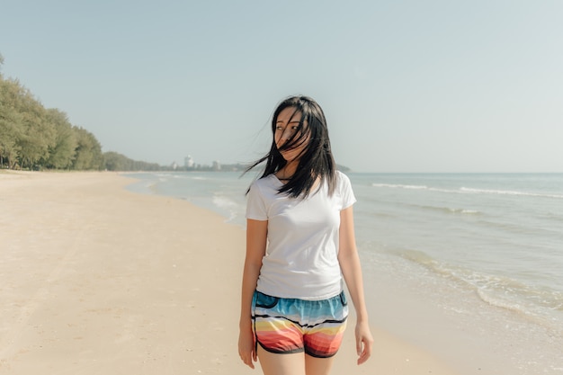 女性は夏の日当たりの良い太陽とビーチの上を歩きます。