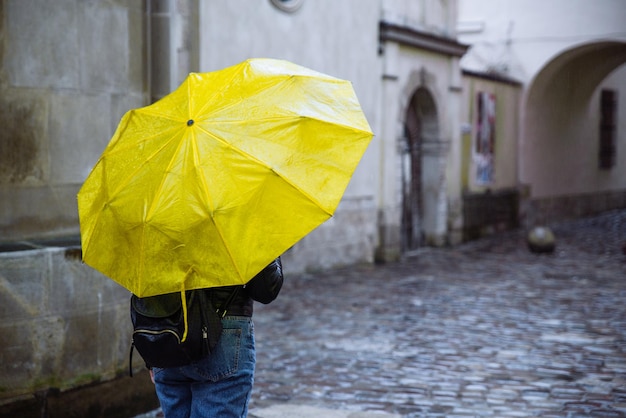 여자는 노란 우산을 들고 비오는 날씨에 오래된 유럽 거리를 걷습니다. 복사 공간