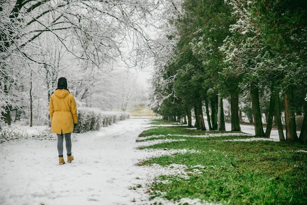 Женщина гуляет по парку, где зима встречает весну