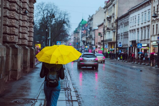 Foto donna camminare a fianco camminare con ombrello giallo tempo piovoso nella vecchia città europea