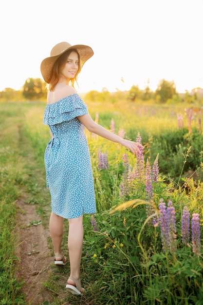 A woman walk the field touches the lupines with her hand and looks at the sunset