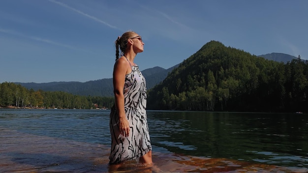 Woman walk on water on pier in sunglasses and a boho silk shawl
girl rest on flood wood underwater dock the pavement is covered
with water in lake