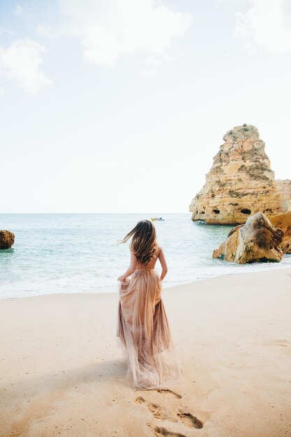 Woman walking along the beach against the rocks and ocean