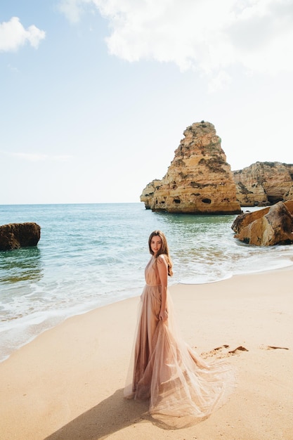 Женщина, идущая по пляжу на фоне скал и океана