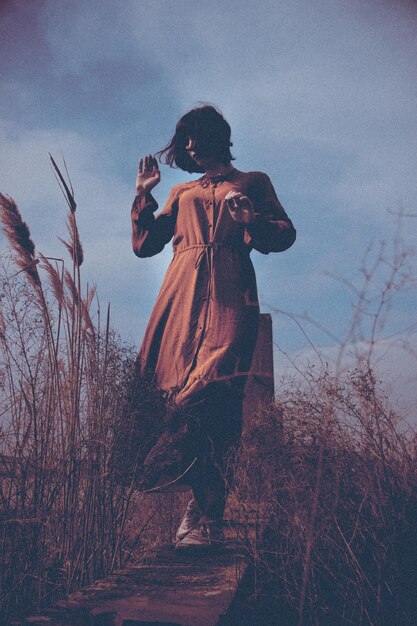 Woman walking amidst plants on field against sky