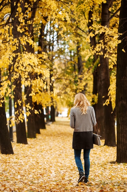 Фото Женщина уходит в осенний парк с золотыми деревьями в полный рост