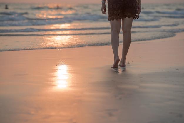 夕暮れ時のビーチを歩いて女性。