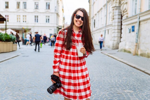 Woman walking by city streets with cool drink and camera