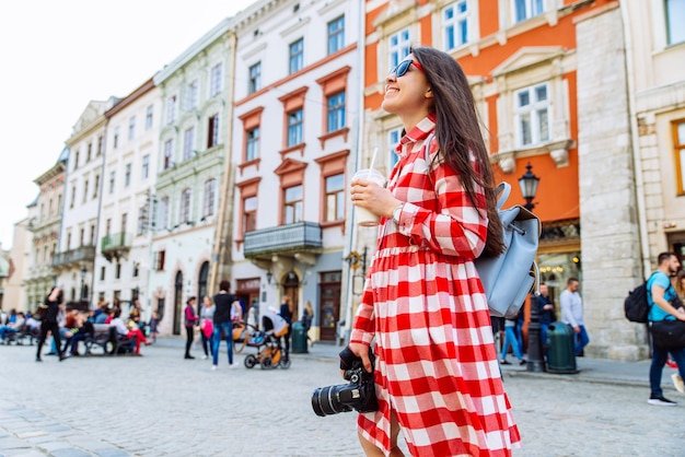 Woman walking by city streets with cool drink and camera