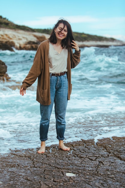 Woman walking by rocky beach in wet jeans barefoot