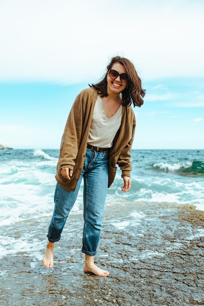 Woman walking by rocky sea beach at sunny windy day summer vacation carefree concept  waves on background