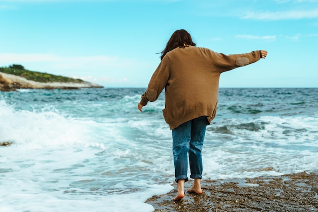 Woman walking by rocky sea beach at sunny windy day summer vacation carefree concept  waves on background