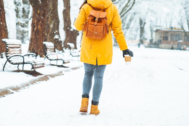 コーヒーカップを手に雪の都市公園を歩いている女性。体の部分。ウォーミングアップ寒い日のコンセプトを閉じる