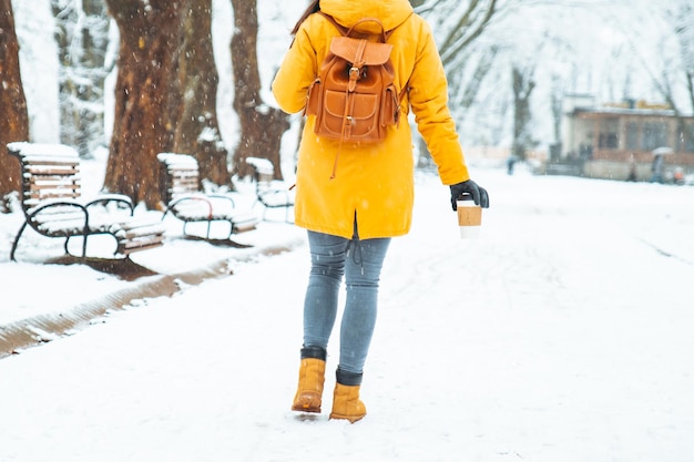 Woman walking by snowed city park with coffee cup in hand. body parts. close up warm up cold day concept