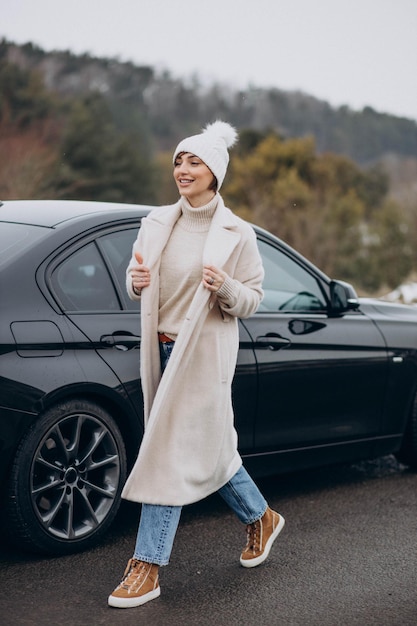 Woman walking cross the road by her car in winter forest